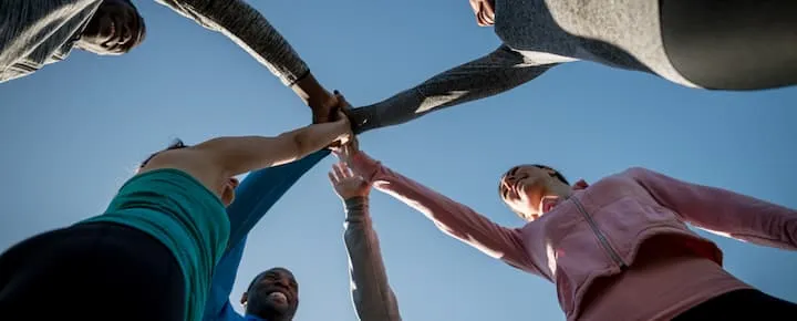 Group of people joining hands in a team huddle outdoors.