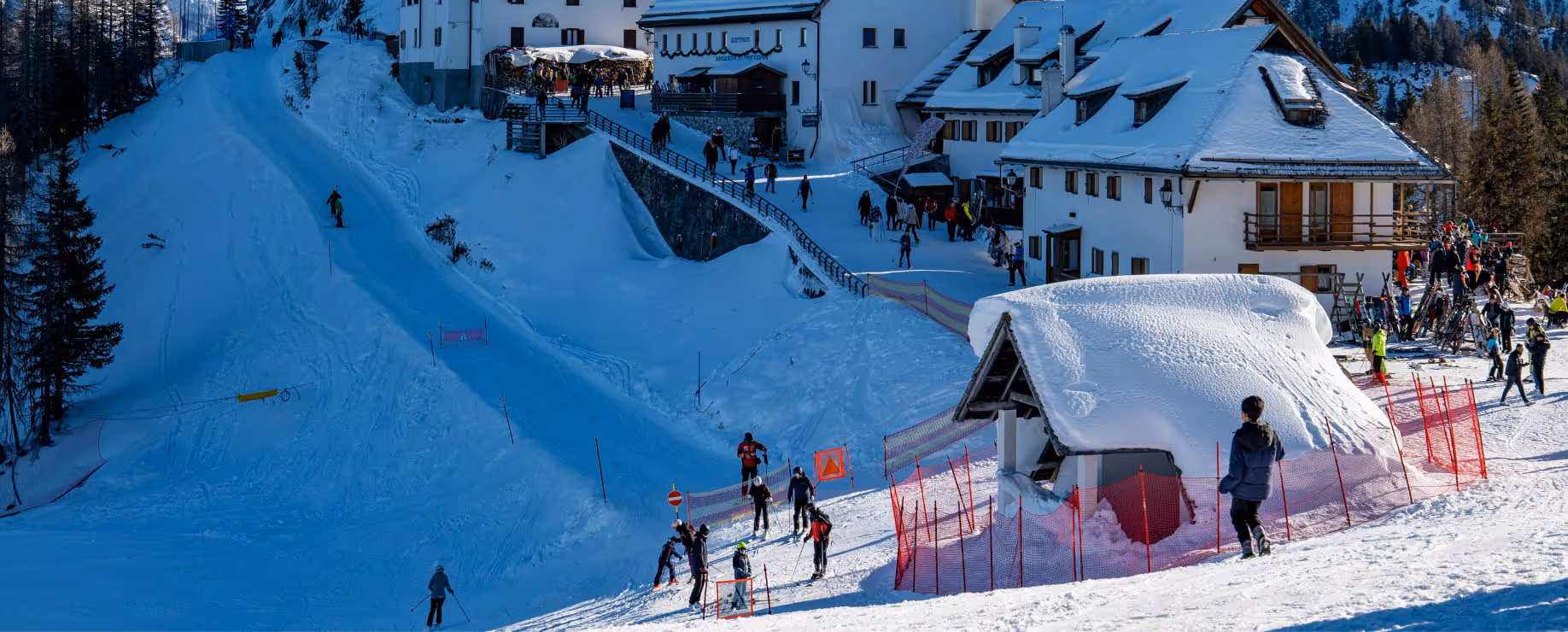 Skiers on a snowy alpine slope with a mountain lodge and red course markers.