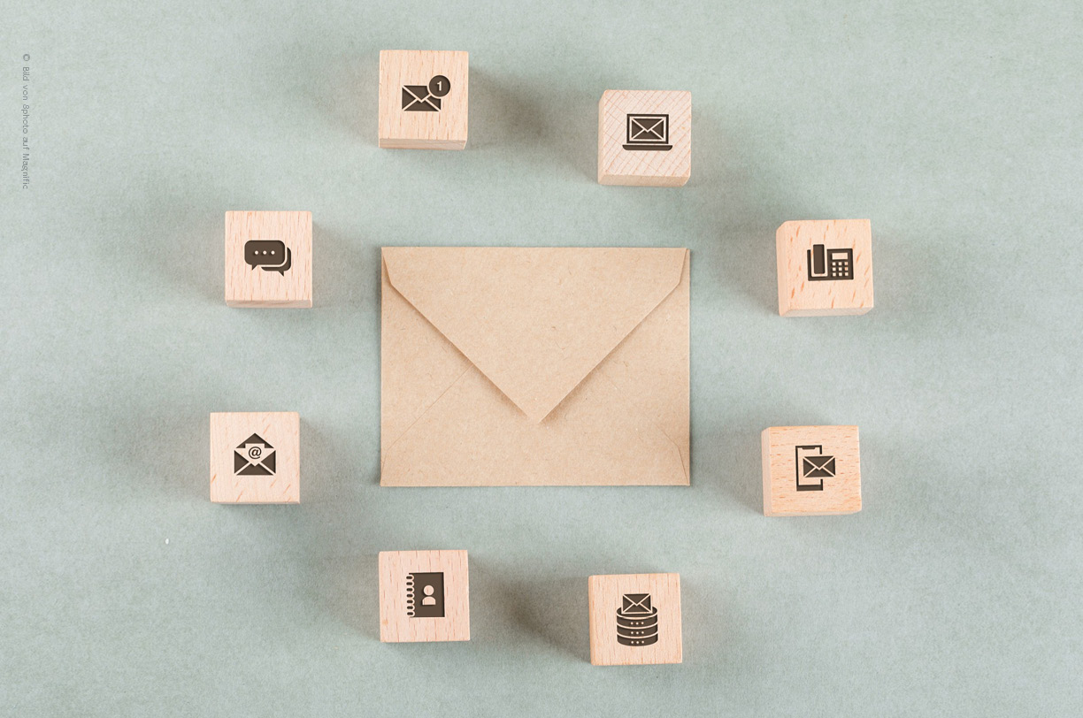 Verschlossener Briefumschlag. Drum herum sind verschiedene Holzklätzchen mit Icons die das Thema E-Mail, Kommunikation und E-Mail-Verschlüsselung symbolisch aufgreifen.