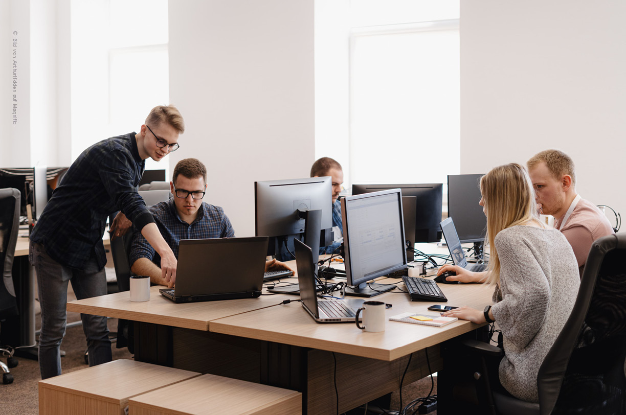 Mehrere IT-Spezialist*innen arbeiten in einem Büro gemeinsam an Bildschirmen, um im Rahmen eines IT-Audits Sicherheitslücken in der IT-Infrastruktur zu identifizieren. 