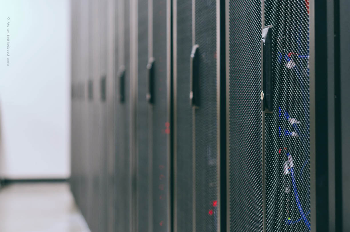 Der Servrraum zeigt ordentlich verkabelte Rcks mit blinkenden Statusleuchten, die eine gut organisierte IT-Infrastruktur repräsentieren. Diese Umgebung ist entscheidend für das IT-Management in Unternehmen, um die Verfügbarkeit und Sicherheit der IT-Systeme zu gewährleisten.