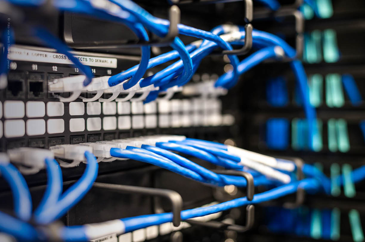 Das Bild zeigt einen Netzwerk-Switch in einem Rechenzentrum, an dem mehrere Kabel angeschlossen sind. Diese IT-Infrastruktur ist entscheidend für den Betrieb und die Verwaltung von Unternehmens-IT-Systemen, da sie die Verbindung zwischen verschiedenen Geräten und Servern ermöglicht.