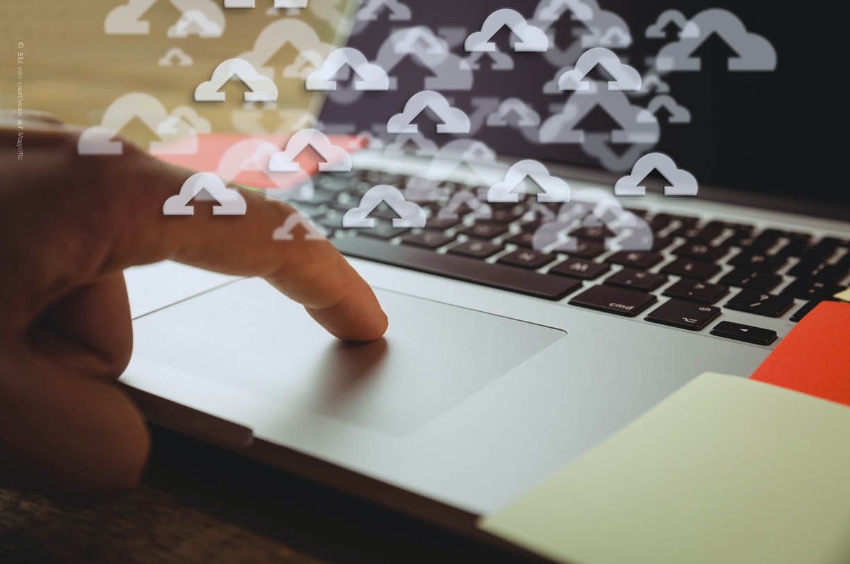 Eine Person tippt auf einem Laptop. Symbolisch sind Upload-Zeichen zu sehen, die für die Daten, die bei einer Cloud-Migration in die Cloud geladen werden, stehen.