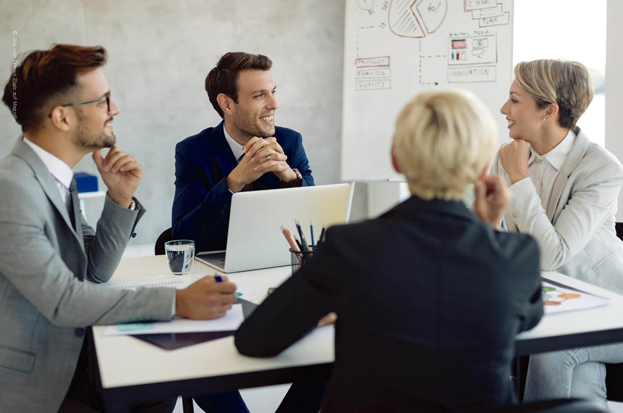 In einem modernen Konferenzraum diskutieren Geschäftsleute die IT-Budgetplanung mit Dokumenten und Laptops. Die Szene zeigt, wie kleine und mittlere Unternehmen die Kosten einer IT-Flatrate mit dem Stundenmodell vergleichen.