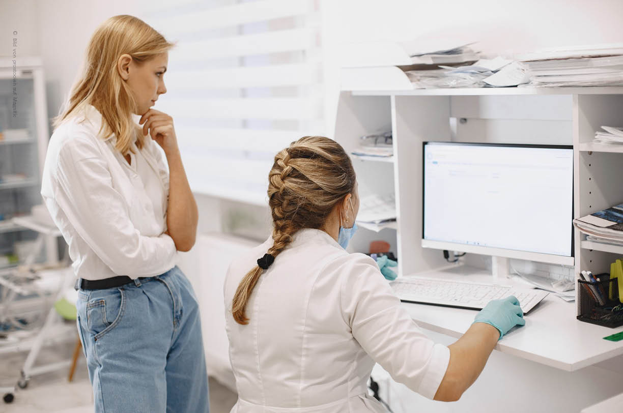In einer modernen Arztpraxis arbeiten eine Ärztin und eine medizinische Assistentin an einem Computerarbeitsplatz, um Patientendaten zu verwalten und die Terminplanung zu optimieren. Die helle Umgebung unterstreicht die Bedeutung von IT-Lösungen und digitaler Unterstützung in der Patientenversorgung.