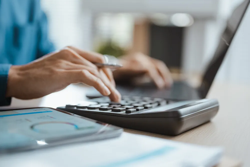 Business professional comparing project management software subscription costs with a calculator and laptop