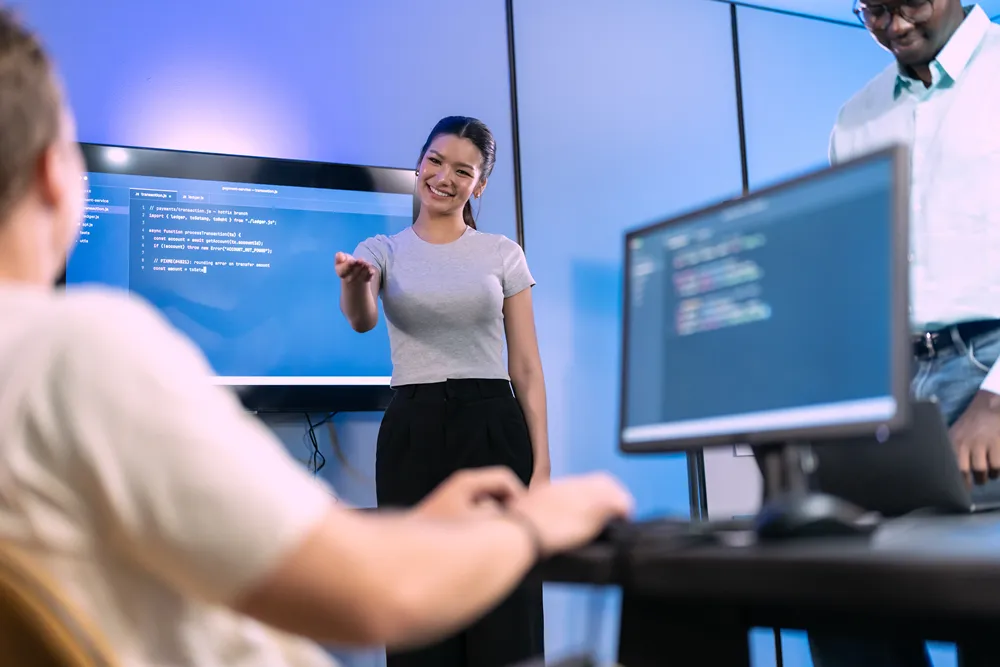 Software development team holding a daily agile standup in front of monitors displaying code