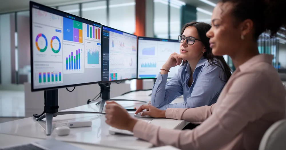 Analytics team reviewing dashboards and reports across multiple monitors for advanced project tracking
