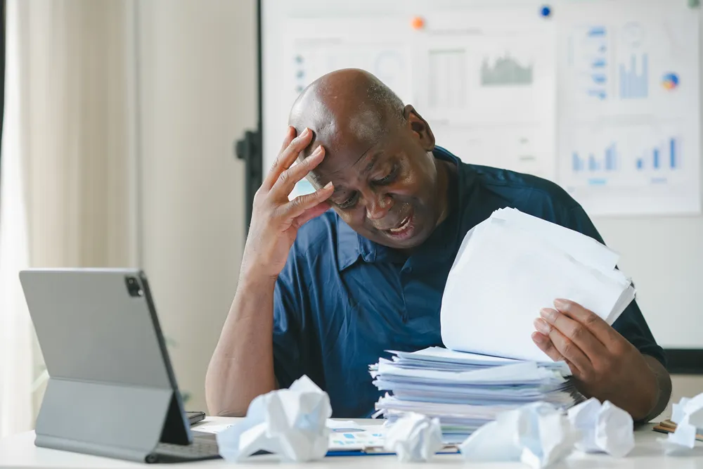 Frustrated employee buried in paperwork and manual data entry before switching to web forms