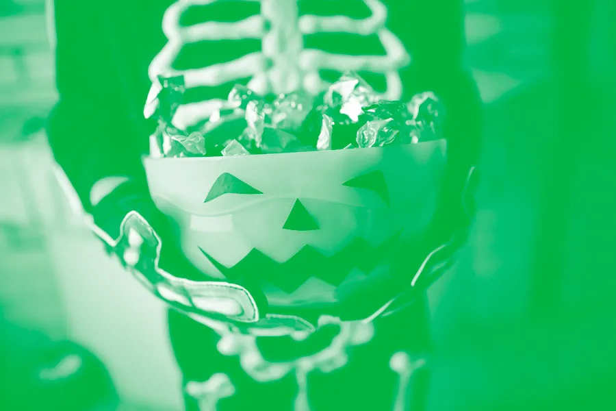 Child in skeleton costume holding full bowl of Halloween candy