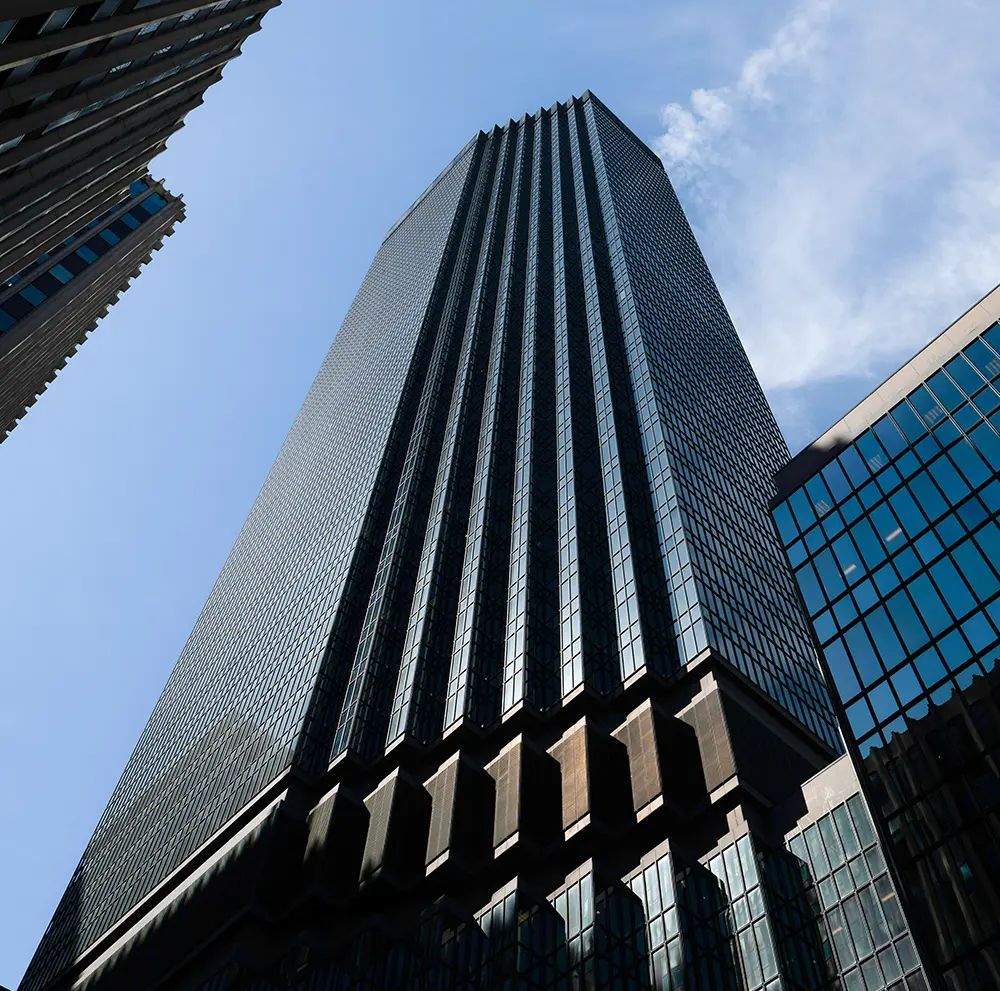 Low-angle view of tall modern skyscraper, IDS Center in Minneapolis, with glass facade under blue sky.