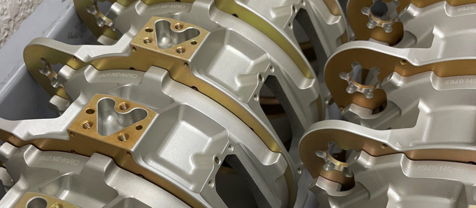 Machined housings staged in bins, each carrying its own OMW serial number