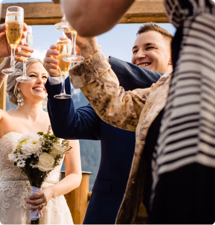 Bride and groom smiling and toasting with champagne glasses during an outdoor wedding celebration.