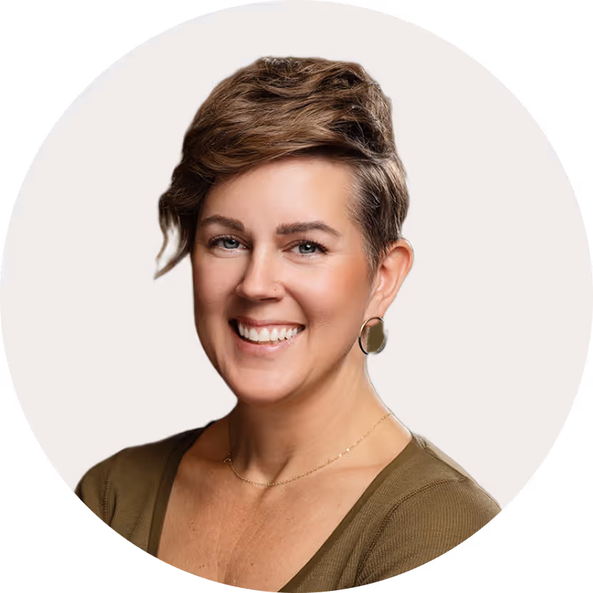 Smiling woman with short, wavy hair wearing a brown top and gold hoop earrings against a light background.