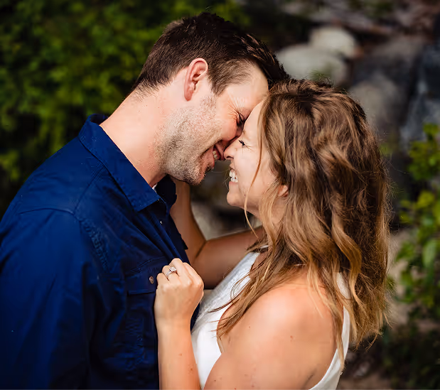 Couple with foreheads touching and eyes closed, smiling closely together outdoors.