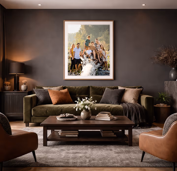 Modern living room with olive green sofa, brown leather chairs, wooden coffee table with flowers and books, and a large framed family photo on a dark gray wall.