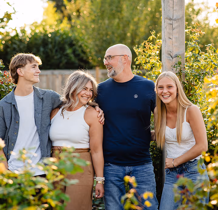 Group of four people, two men and two women, standing close together outdoors surrounded by greenery and smiling warmly.