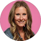 Smiling woman with long wavy blonde hair wearing a denim jacket against a pink background.