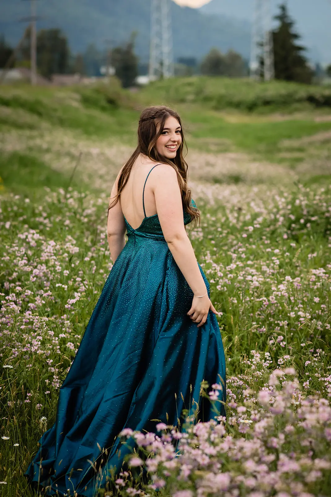 Smiling woman in a shimmering blue gown standing in a field of wildflowers.