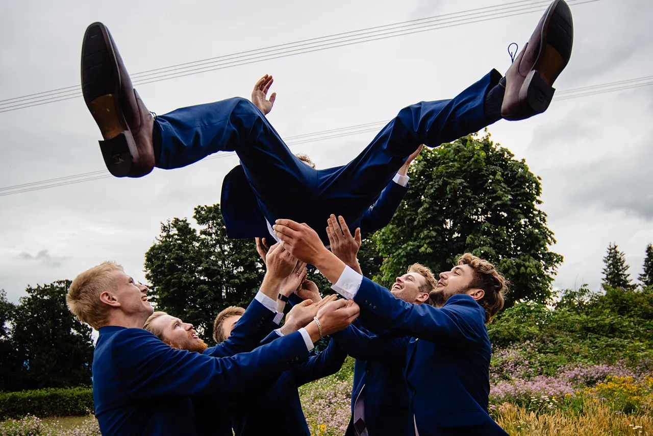 Group of men in blue suits tossing another man in blue suit into the air outdoors.