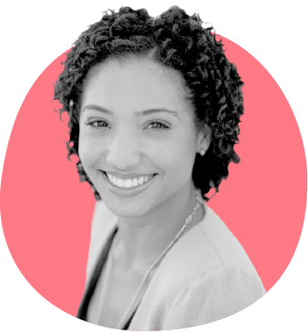 Smiling woman with curly hair wearing a light blazer, against a pink circular background.