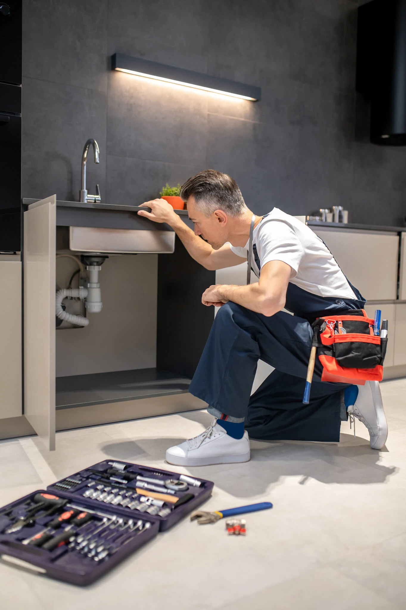 Licensed plumber crouching beside a kitchen sink with an open emergency plumbing toolbox ready for urgent repairs in a GTA home by Galaxy Plumbing
