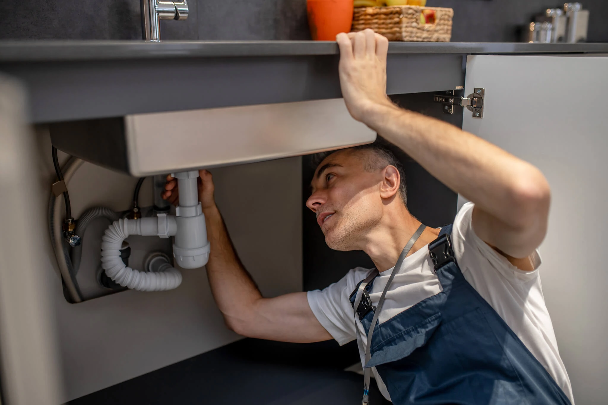 Plumber inspecting pipes under a kitchen sink for a potential sewer line clog