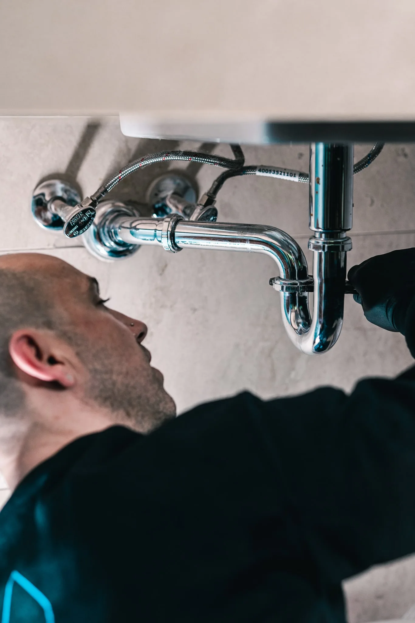 Plumber inspecting the P-trap and drain pipes beneath a kitchen sink for a blockage