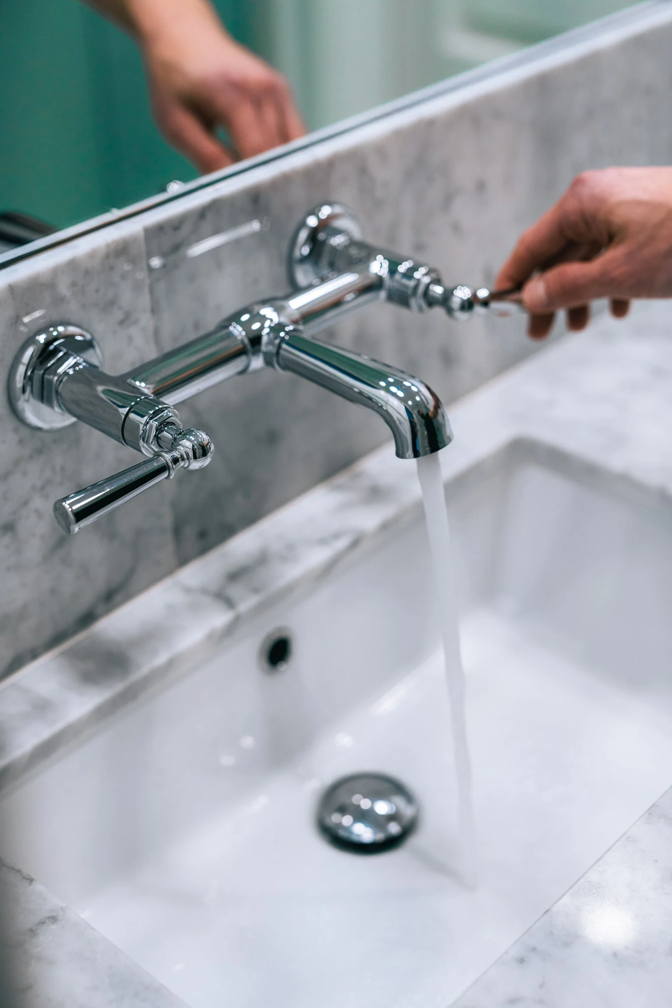 Clean water flowing from a wall-mounted faucet into a white residential sink basin