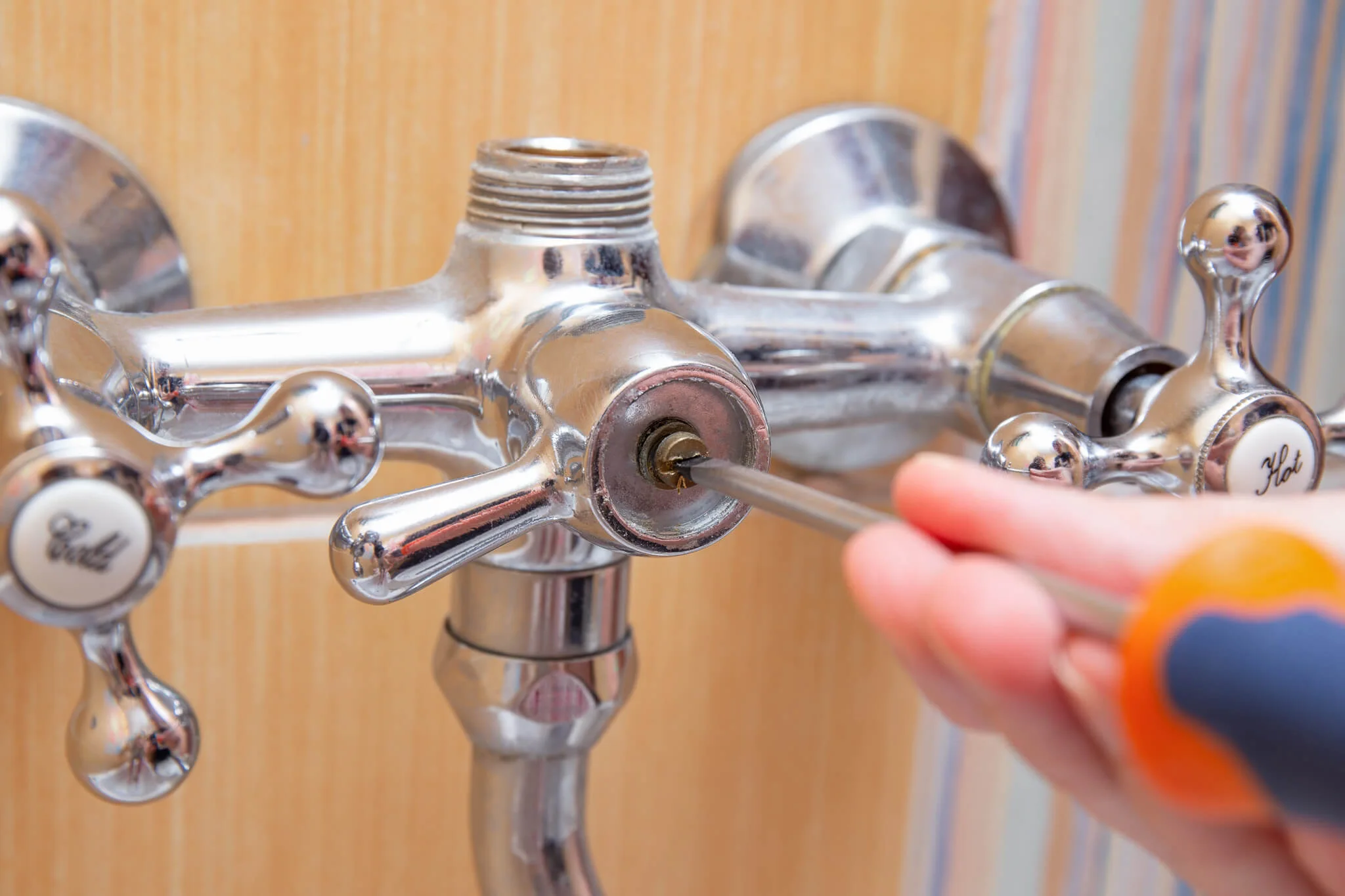 Person using a screwdriver to repair a shower valve body and handles in a residential bathroom