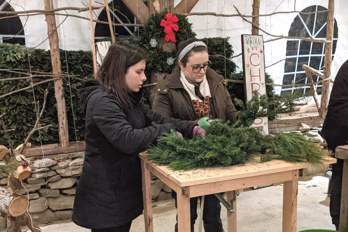 Two woman making wreaths using our custom wreath making tables.