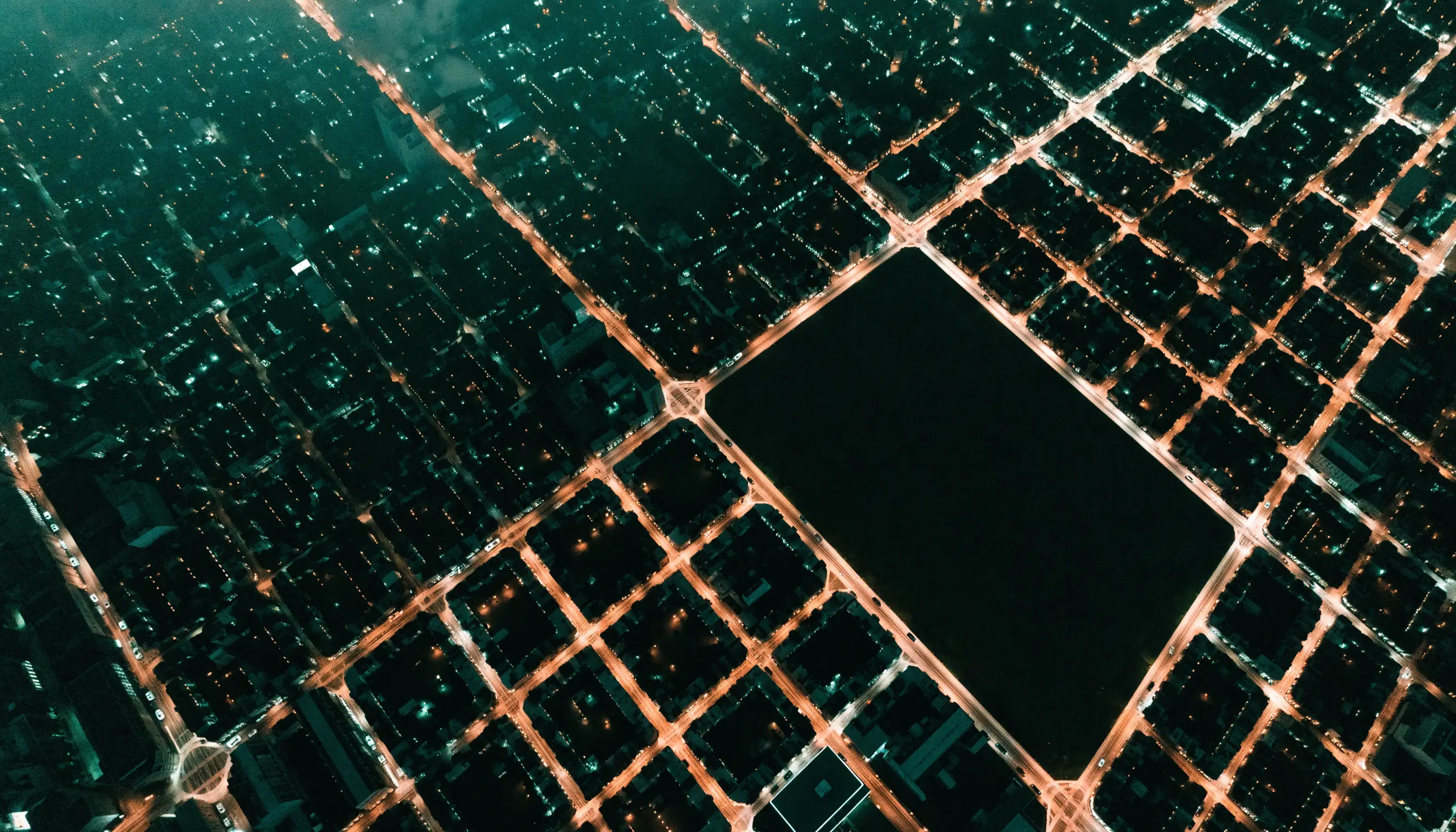 Aerial night photograph of a lit city grid with one rectangular district completely dark, representing a geographic holdout region in an incrementality test
