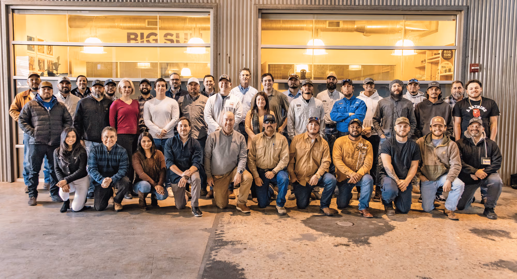 Group photo of 33 diverse men and women posing inside a warehouse with 'BIG SUN' visible inside behind them.