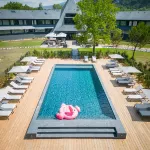 Piscine extérieure de l’Hôtel Miura entourée de transats, au cœur d’un parc arboré près du lac du Bourget