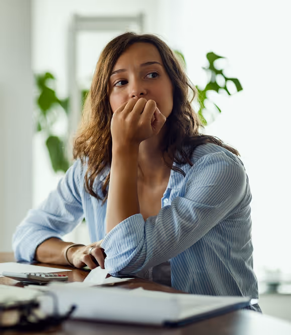 young woman biting her nails looking off camera at a desk