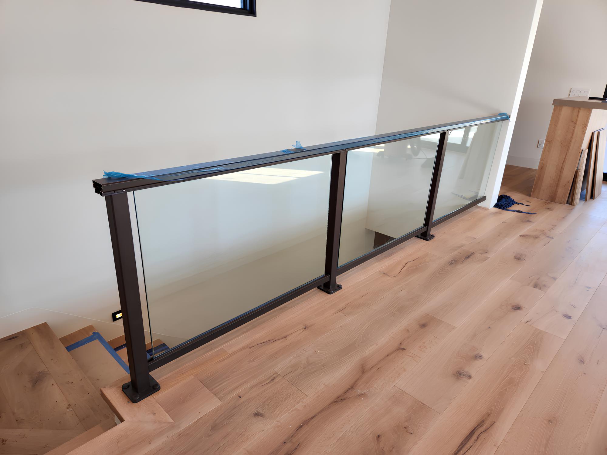 Glass stair railing with metal frame on wooden floor in modern interior space.