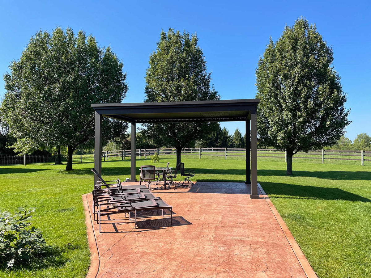 Outdoor patio with lounge chairs and a pergola amid green lawn and trees under clear sky.