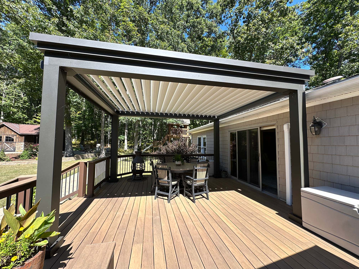 Outdoor deck with a pergola, table, four chairs, and surrounding trees on a sunny day.