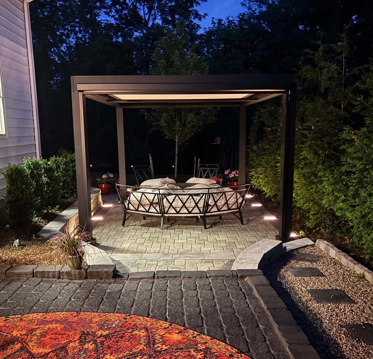 Outdoor patio gazebo with cushioned metal chairs under soft lighting at night.