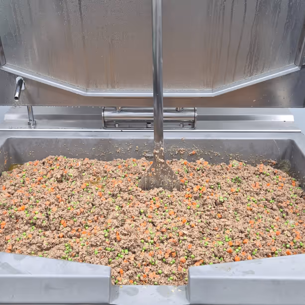 Freshly cooked dog food being cooked in a large stainless steel pan, with visible peas, carrots, and beef.