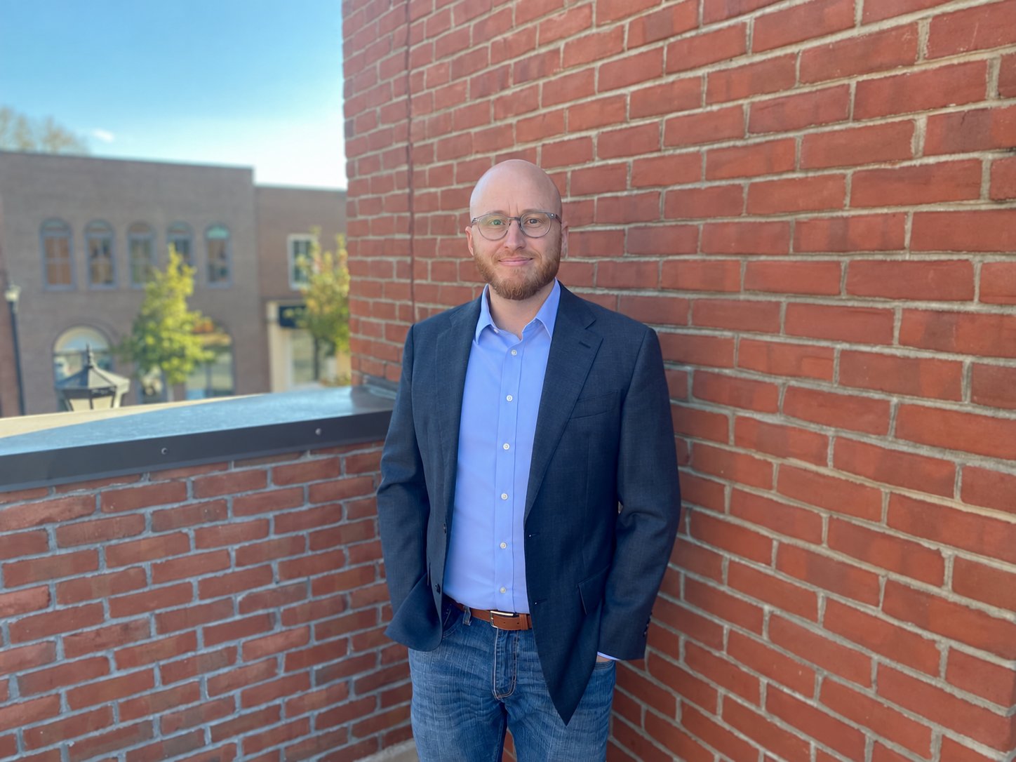 Tyler Wallace, Ph.D., in a navy blazer standing against a red brick wall downtown