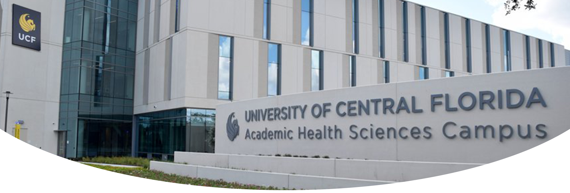 A large concrete sign for the University of Central Florida Academic Health Sciences Campus standing in front of a modern, multi-story campus building.