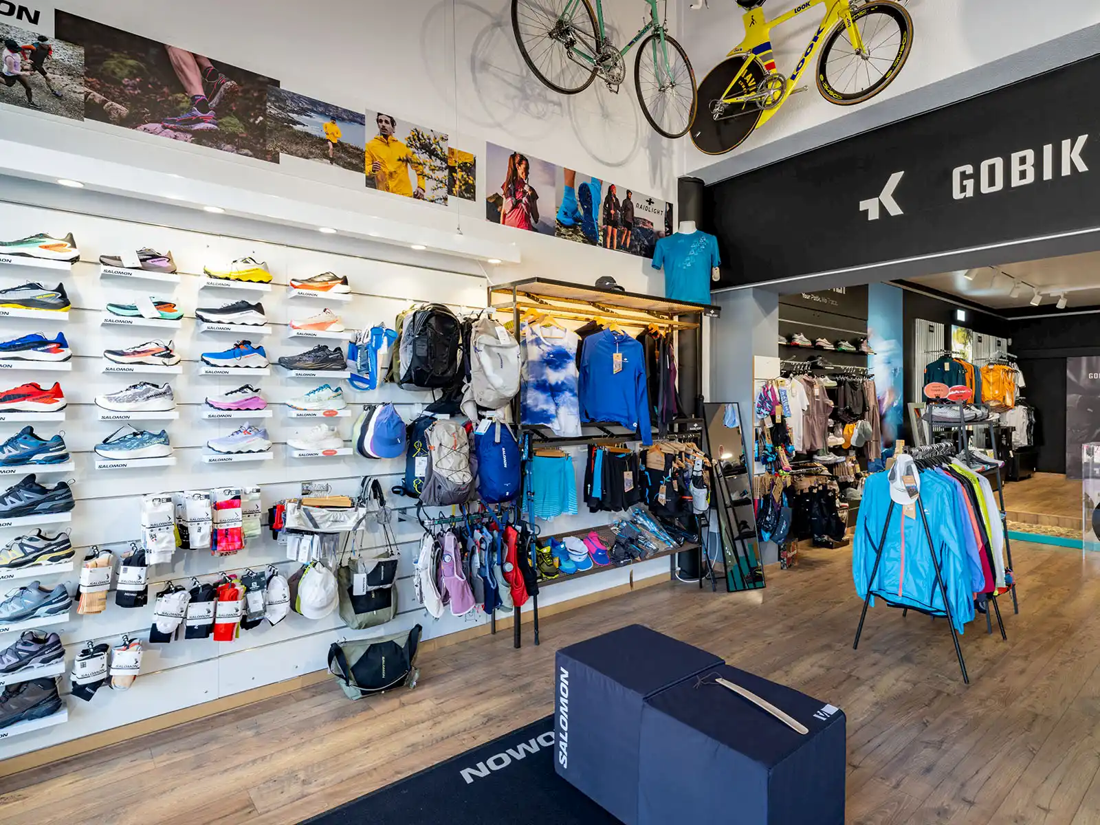 Innenansicht eines Sportgeschäfts mit ausgestellten Laufschuhen, Rucksäcken und Sportbekleidung sowie aufgehängten Fahrrädern an der Decke.