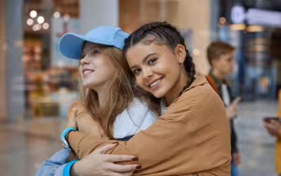Two young teenage girls smiling and hugging in a shopping centre. Life insurance for people with diabetes.