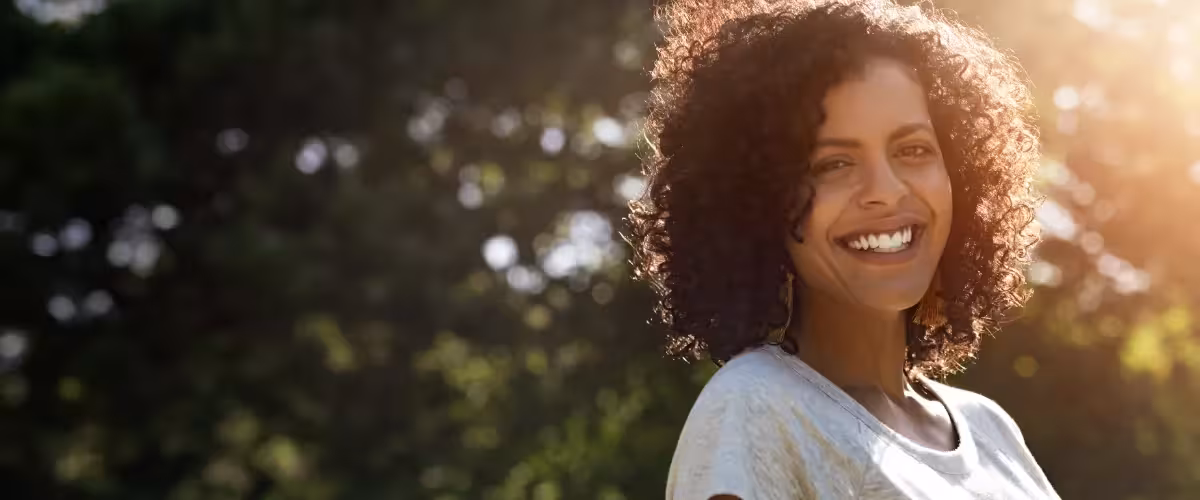 image of smiling woman outside in the sun and trees in background