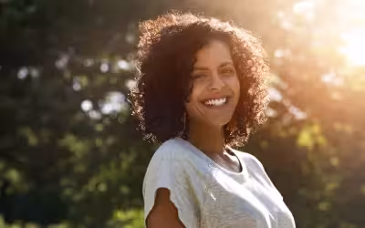 image of smiling woman outside in the sun and trees in background