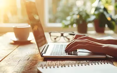 Person typing on a laptop at a wooden desk. Cost of private carpel tunnel surgery.