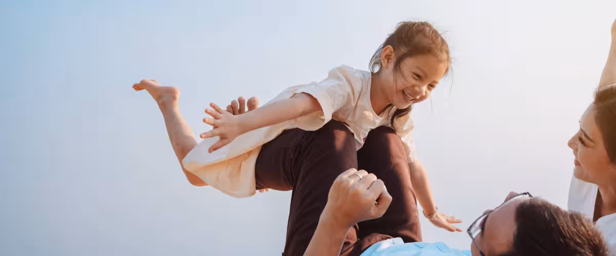 Smiling, young family on a picnic blanket in a park, small daughter is 'flying' on fathers legs. Is life insurance taxable?