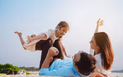 Smiling, young family on a picnic blanket in a park, small daughter is 'flying' on fathers legs. Is life insurance taxable?