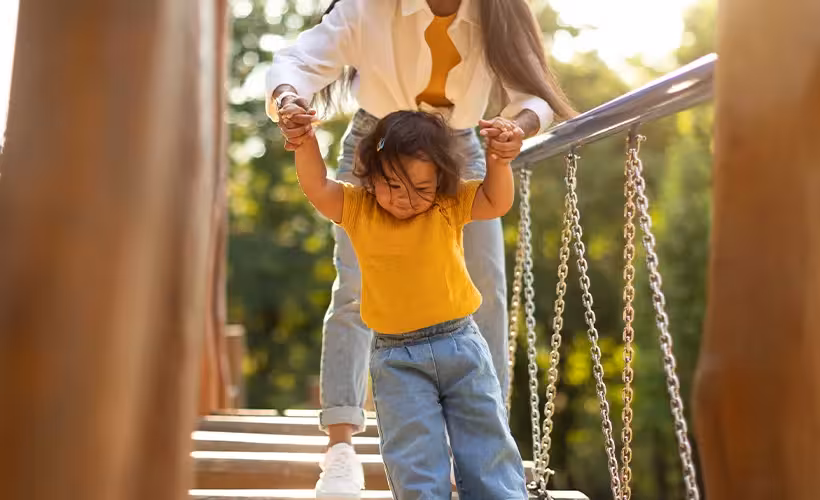 Mommy Holding Daughter's Hands Walking Swinging Bridge On Playground